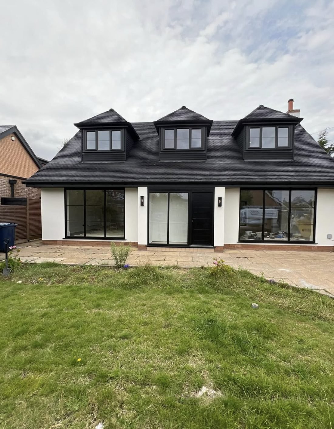Rear of a chalet house in white render with three dark dormers and full-height glazing