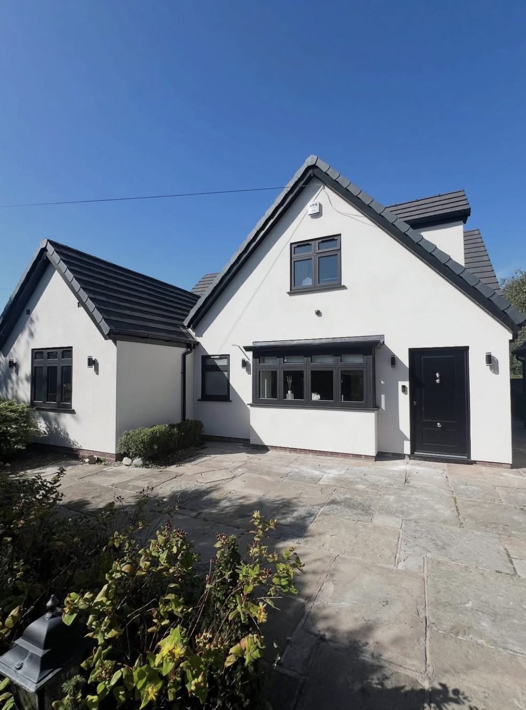 White rendered house with steep gables, dark window frames and a paved drive