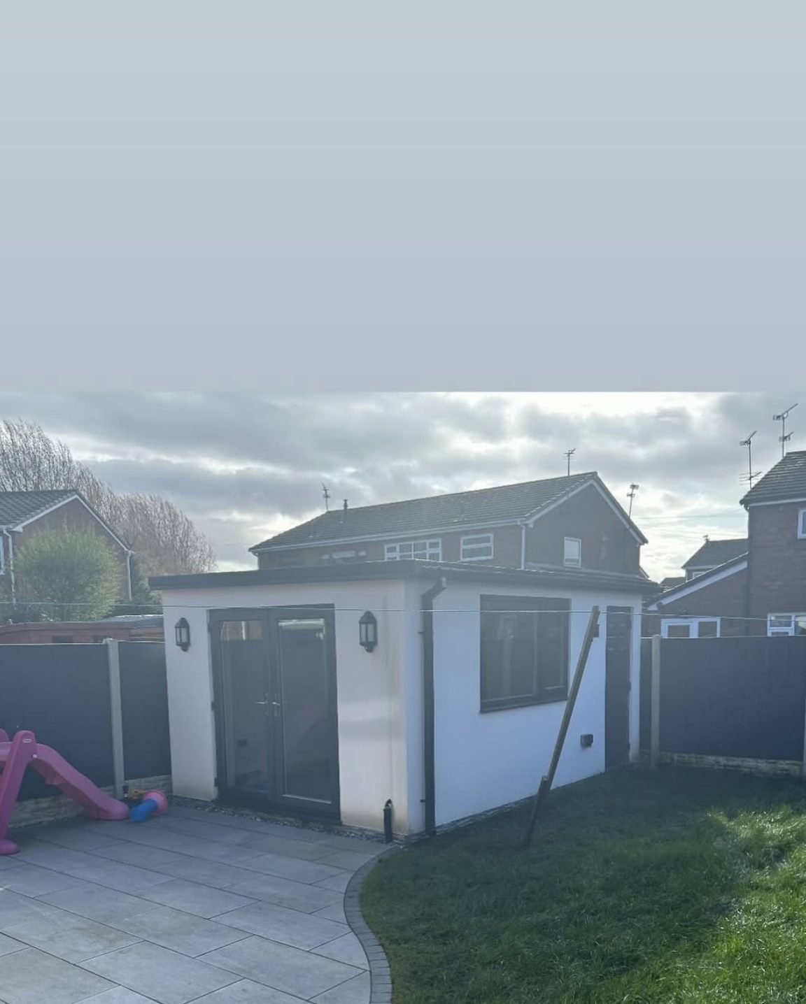 Small rendered outbuilding with a grey door at the end of a garden