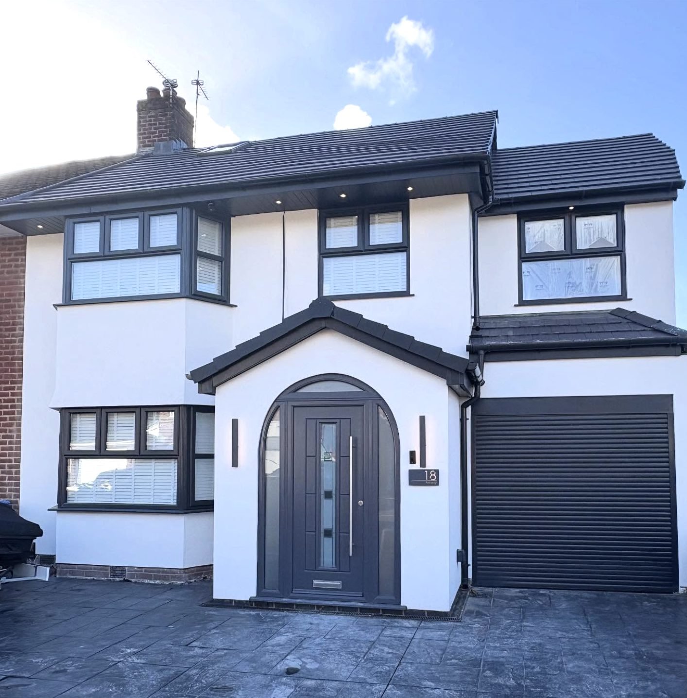 Semi-detached house in white render with an arched porch, grey door and garage