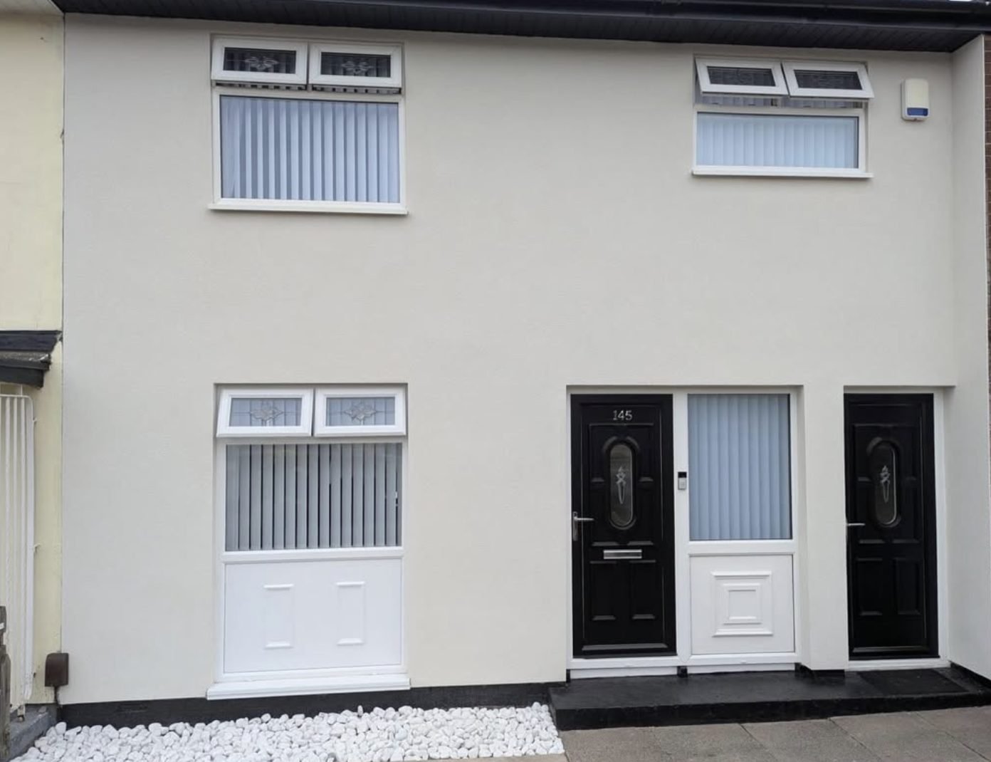 Flat-fronted terraced houses finished in smooth cream render with black doors