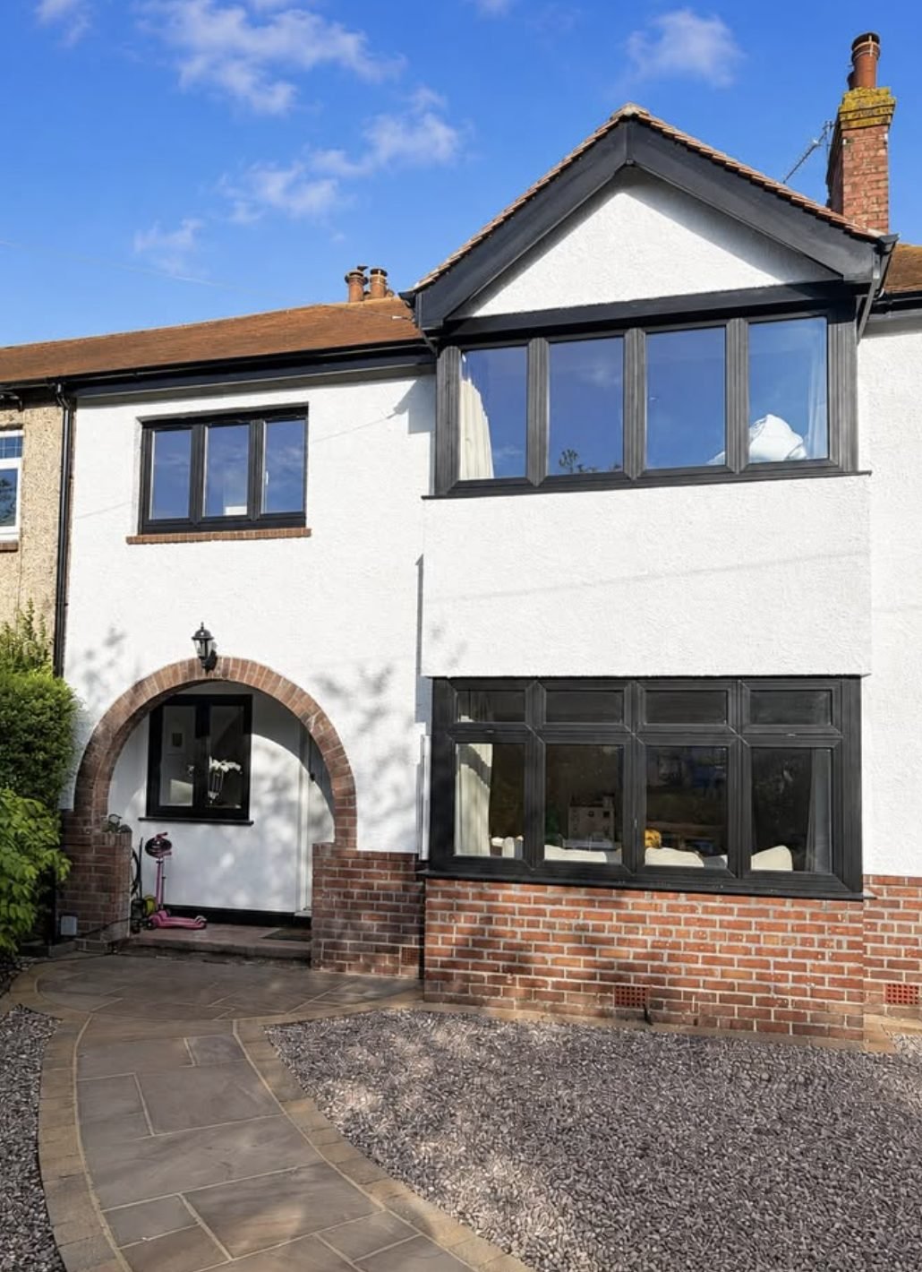 Terraced house in white render with a gabled bay, arched brick porch and brick plinth