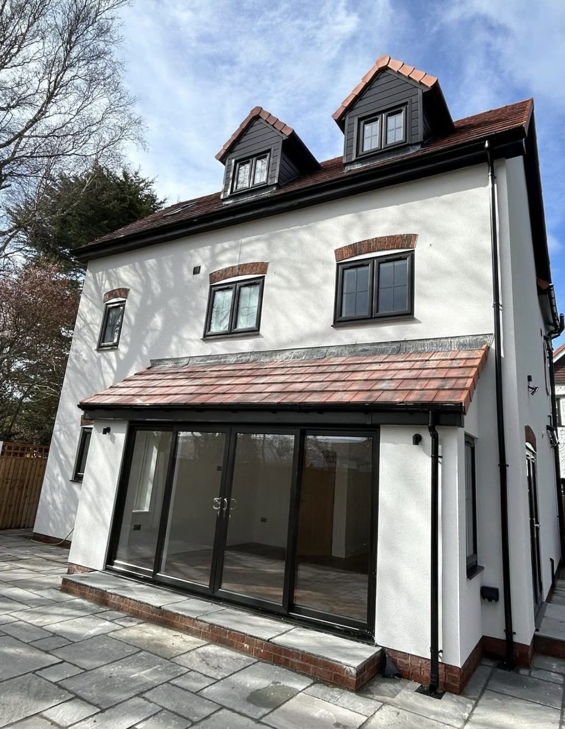 Three-storey rear elevation in white render with two dormers and a tiled extension with bifold doors