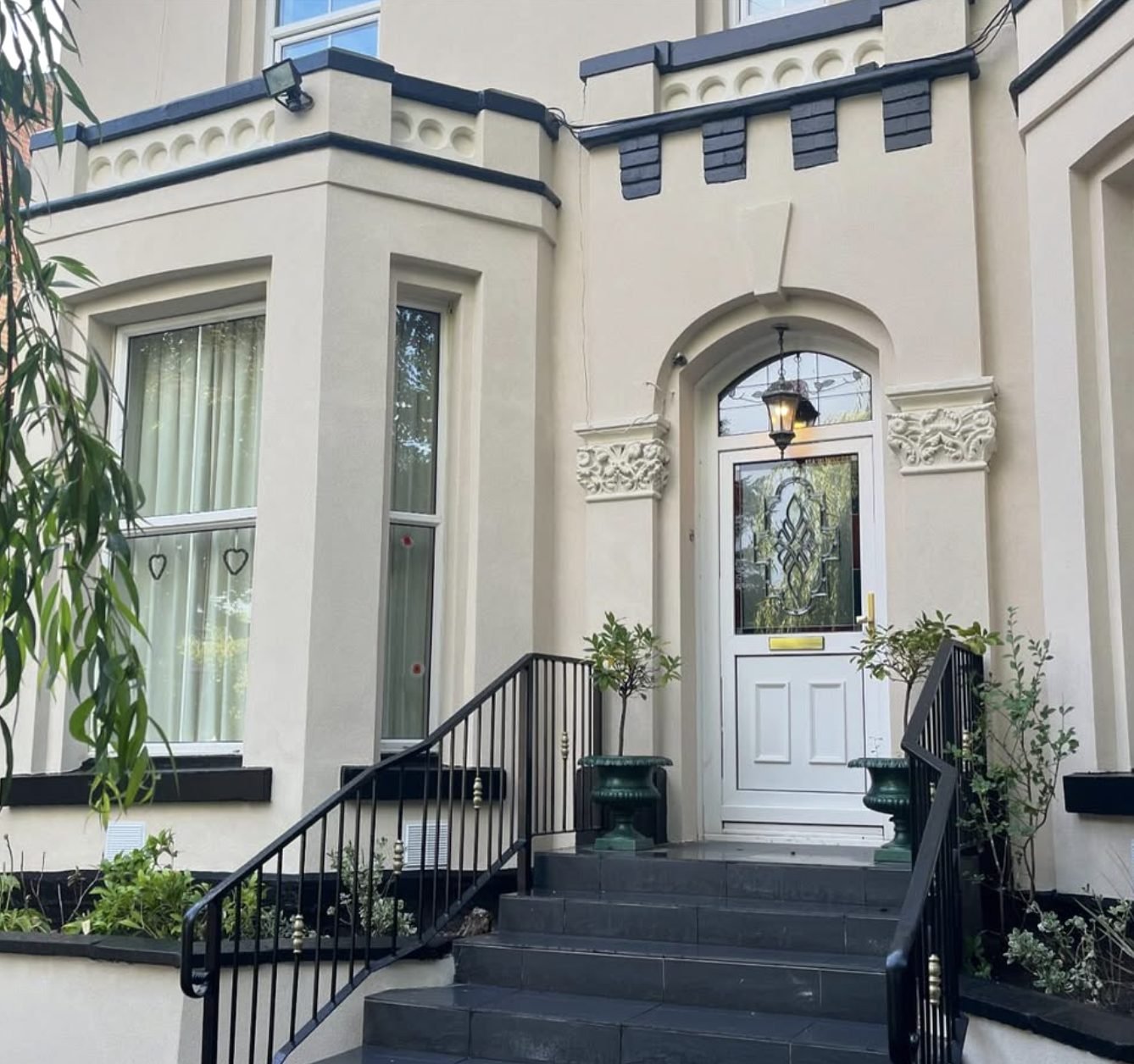 Victorian bay-fronted house with cream stucco, decorative door surround and black railings up the front steps
