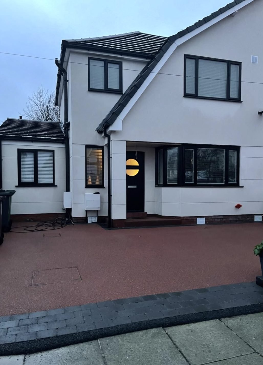 White rendered house with black window frames and a red block-paved drive